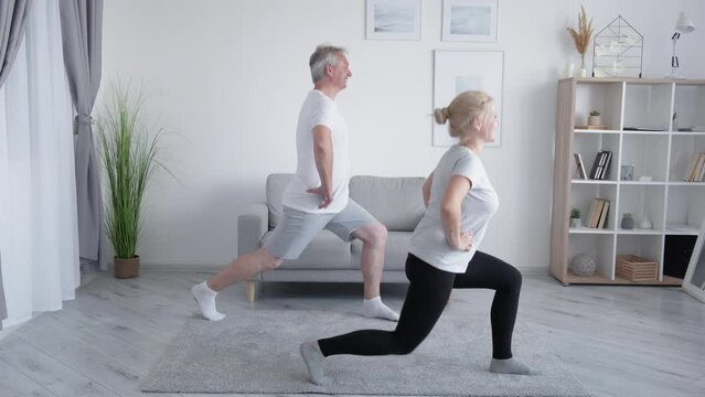 Family training. Home fitness. Active people. Inspired smiling daughter middle-aged father enjoying doing legs strengthening lunge exercise together in modern interior.