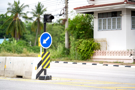 A Thailand road sign white arrow on the blue circle plate standing alone far away to indicate which direction should go between barricade left or right way.