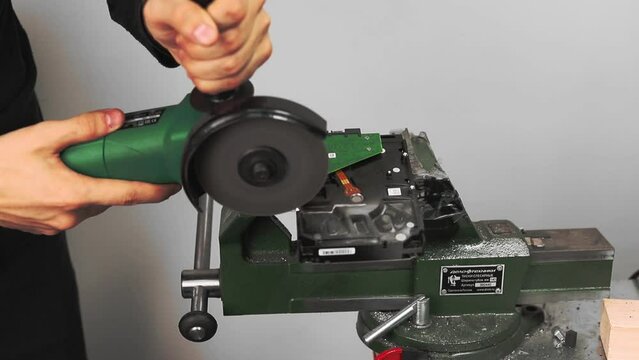 KAZAN, TATARSTAN RUSSIA - MARCH 03 2020: Worker cuts hard disk drive in clamp with circular saw in workshop closeup. Reusing old computer details process on March 03 in Kazan
