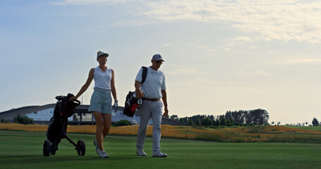 Obraz premium Couple golf players discuss sport course outside. Two golfers walk grass field.