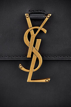 Yves Saint Laurent logo in the form of the letters ISL made of gold metal on the leather strap of the bag made of black leather. Advertising shooting, Belarus, Minsk, 03.02.2022.