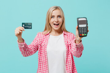 Young happy excited woman she 30s in pink shirt white t-shirt hold wireless modern bank payment terminal to process acquire credit card payments isolated on plain pastel light blue background studio.