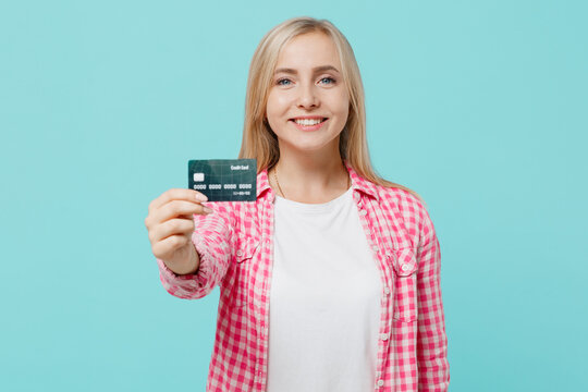 Young happy smiling fun cool caucasian woman she 30s in pink shirt white t-shirt hold in hand credit bank card isolated on plain pastel light blue background studio portrait. People lifestyle concept.