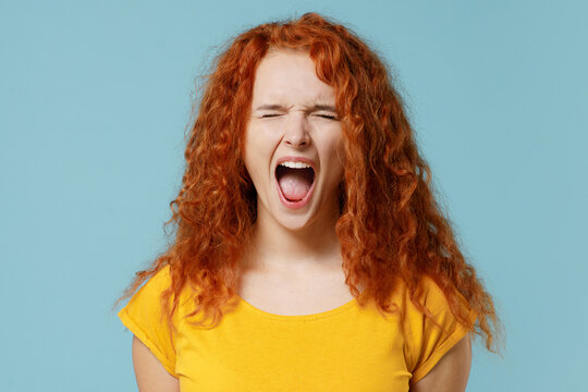 Young stressed mad sad caucasian redhead woman 20s wearing yellow t-shirt close eyes screaming shouting isolated on plain light pastel blue color background studio portrait. People lifestyle concept.
