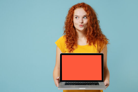 Young minded happy redhead woman 20s in yellow t-shirt hold use work on laptop pc computer with blank screen workspace area look aside on workspace area isolated on plain light pastel blue background