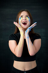  Indoor  portrait of crying young girl with blue and yellow ukrainian flag tears on her cheek ....