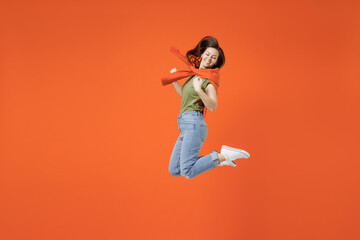Obraz premium Full body young smiling cool happy woman 20s wearing khaki t-shirt tied sweater on shoulders jump high do winner gesture isolated on plain orange background studio portrait. People lifestyle concept.