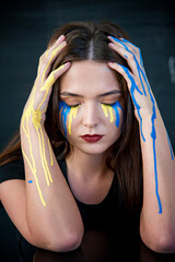 Indoor  portrait of young girl with blue and yellow ukrainian flag tears on her cheek . Freedom...