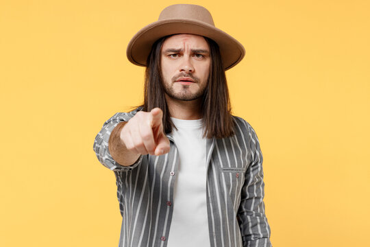 Young strict angry man he 20s wears striped grey shirt white t-shirt hat point index finger camera on you say do it isolated on plain yellow color background studio portrait. People lifestyle concept.
