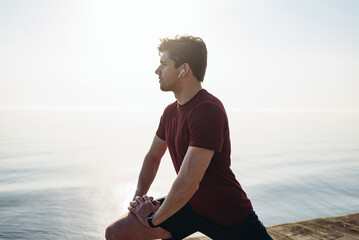 Side view young strong sporty athletic fit sportsman man in sports clothes do squates listen music...