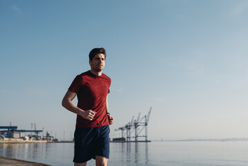 Young active strong sporty athletic toned fit sportsman man 20s wear sports clothes earphones listen music run warm up training at sunrise sun dawn over sea beach outdoor on pier seaside in morning.