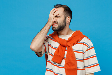 Young caucasian man 20s in orange striped t-shirt looking camera put hand on face facepalm epic fail mistaken omg gesture isolated on plain blue background studio portrait. People lifestyle concept.