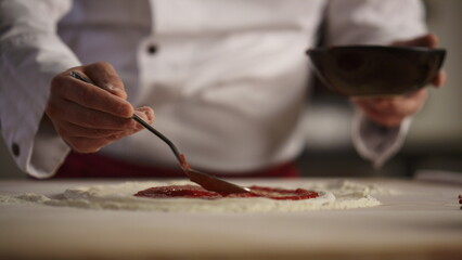 Chef making italian pizza in restaurant. Cook spreading tomato sauce in kitchen.