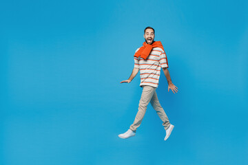 Fototapeta na wymiar Full body side profile view young smiling surprised cheerful man 20s wearing orange striped t-shirt walking going jump high isolated on plain blue background studio portrait. People lifestyle concept.