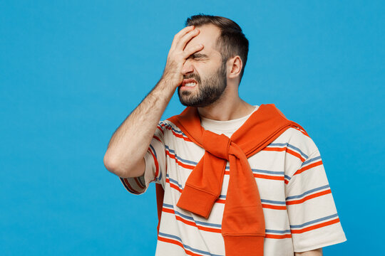 Young caucasian man 20s in orange striped t-shirt looking camera put hand on face facepalm epic fail mistaken omg gesture isolated on plain blue background studio portrait. People lifestyle concept.