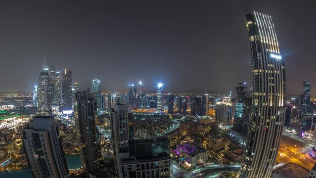Aerial panoramic view of a big futuristic city during all night timelapse. Business bay and Downtown district with many skyscrapers and traditional houses with lights turning off, Dubai, United Arab