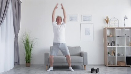 Home fitness. Indoor training. Active lifestyle. Inspired athletic middle-aged man doing jumping jack cardio exercise in light living room interior.