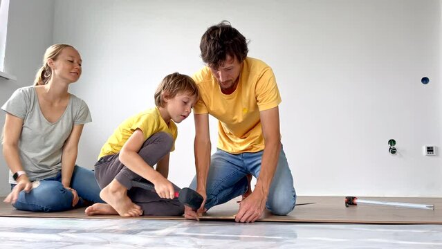 A family of mother, father and son install laminate on the floor in their apartment. DIY concept. Slowmotion video