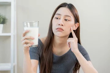 Fotobehang Allergy asian young woman, girl looking, holding glass of milk, face in thinking before drink milk as it may upset her stomach ache, pain. Lactose intolerance and dairy food , health problem concept. © KMPZZZ