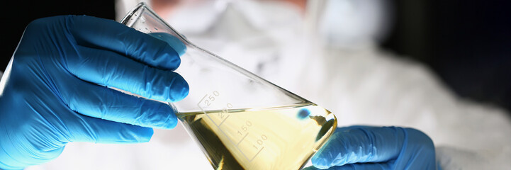 Laboratory pharmacist in respirator analyzing flask with yellow liquid