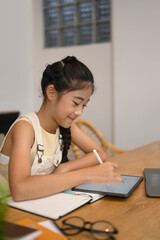 Smiling Asian girl doing homework on digital tablet, studying through online learning system