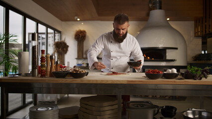 Man cooking italian pizza in restaurant. Chef spreading tomato sauce in kitchen.
