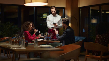 Couple paying restaurant bill on night date. Waiter serving customers in cafe.