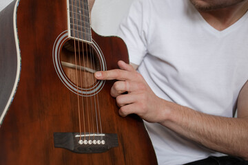A man in a white T-shirt touching a guitar