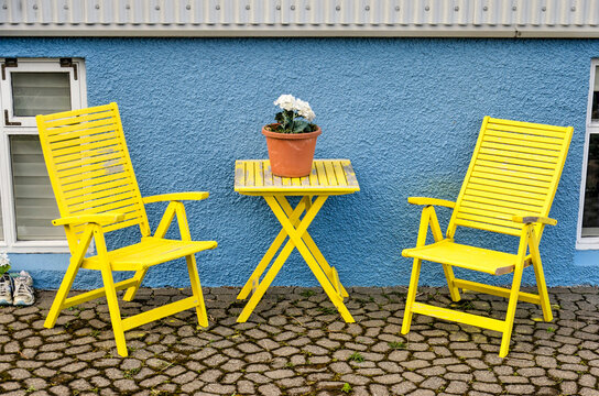 Stykkisholmur, Iceland, May 3, 2022: two yellow wooden chairs and ditto table on a terrace in front of the wooden plaster facade of a house