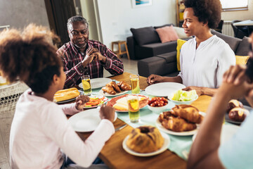 A multi-generational African-American family enjoying food at their dinner table.