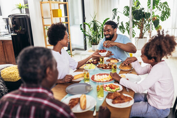 A multi-generational African-American family enjoying food at their dinner table.