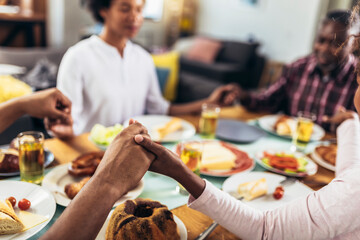 A multi-generational African-American family saying grace at dinner table and holding hands