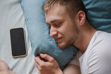 A man is asleep in bed with his phone next to him.