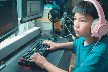 Asian kid is coding and scripting program on on his game streaming desktop computer with headphone on. - 510545953