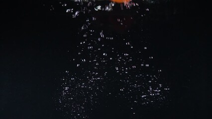 Red bell pepper falls down in clear water with bubbles spreading on black background. Fresh ripe vegetable thrown into water macro slow motion - Powered by Adobe
