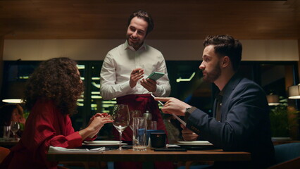 Smiling waiter serving couple on restaurant date. Mixed race lovers in cafe bar.