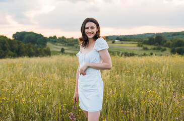 young happy female walking in the field enjoying beautiful sunset. Beautiful countryside. Slow living concept