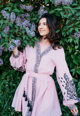 vertikal portrait of young beautiful female standing near the blossoming lilac tree wearing vyshyvanka - ukrainian national clothes. 