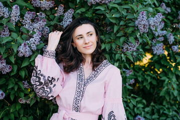 horizontal portrait of young beautiful female standing near the blossoming lilac tree wearing vyshyvanka - ukrainian national clothes. 