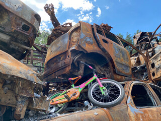 An old children's bicycle in a car graveyard. The consequences of the war in Ukraine.