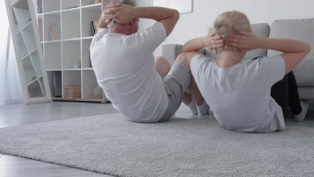 Family fitness training. Home gym. Body sculpt. Healthy leisure. Couple doing abs sit-up exercise together with couch in light interior.