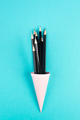 Black pencils in a cone on a blue background, minimalism, creative, surreal and education concept,...
