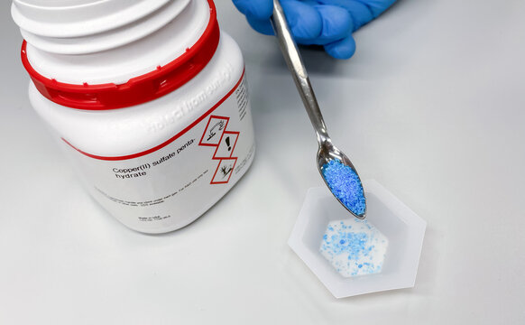 Copper sulfate pentahydrate (CuSO4 x 5H2O) while weighing in by a scientist in chemical laboratory. The compound is a corrosive agent that possess health risk and is toxic to environment.