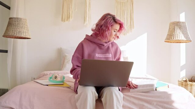 Teen girl using laptop computer sitting in bed distance learning online.
