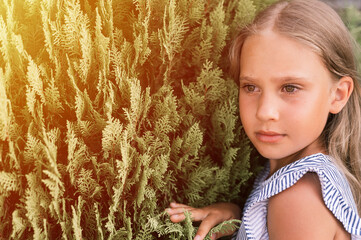 portrait face of candid happy little kid girl of eight years old with long blond hair and green eyes on background of green plants during a summer vacation travel. gen z mental health concept. flare