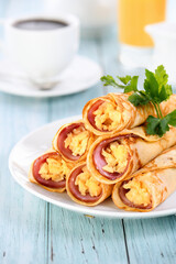 Homemade thin pancakes with a slice of ham and scrambled eggs, stacked in a stack, on the table. Great breakfast idea.