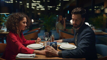 Flirting couple hold hands in restaurant. Man kissing girlfriend on dinner date.