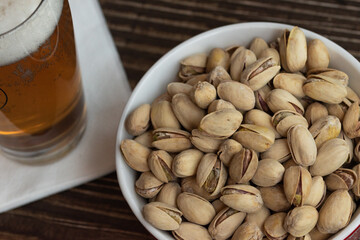 Pistachos con cáscara y cerveza sobre una mesa de madera oscura.