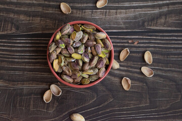 Pistachos pelados en un bol sobre una mesa de madera oscura.