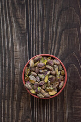 Pistachos pelados en un bol sobre una mesa de madera oscura.